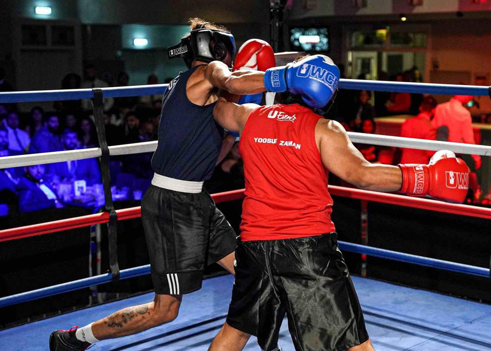 Co-founder Yoosuf Zaman, in a red vest with his name printed across the back, landing a punch in the ring at a fight night.