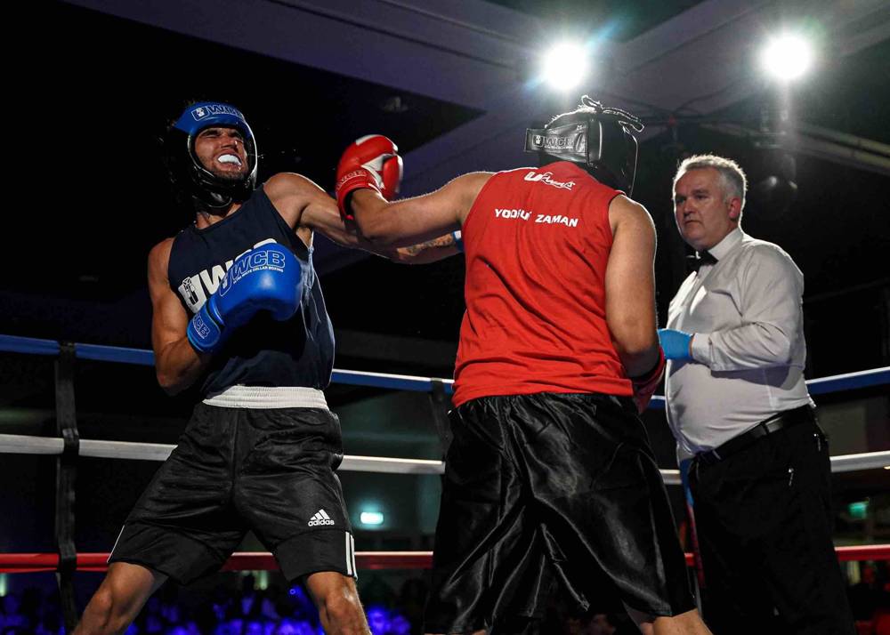 A fight night bout under venue lights: two fighters exchanging in the ring while the referee watches.